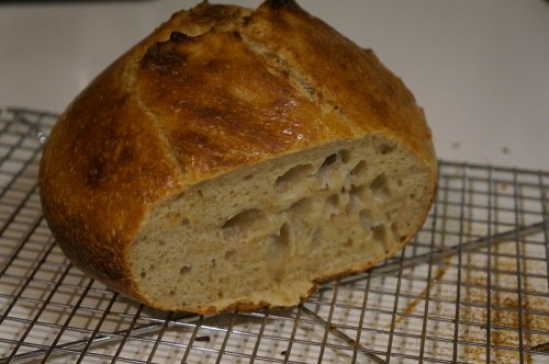 A freshly baked round loaf of bread, partially sliced, resting on a wire cooling rack.