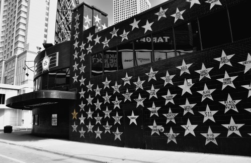 A black and white photo of a building wall covered in stars, each featuring names of various music artists.