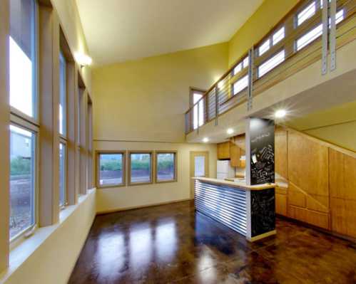 Modern kitchen and living area with high ceilings, large windows, and wooden accents. Bright and spacious design.