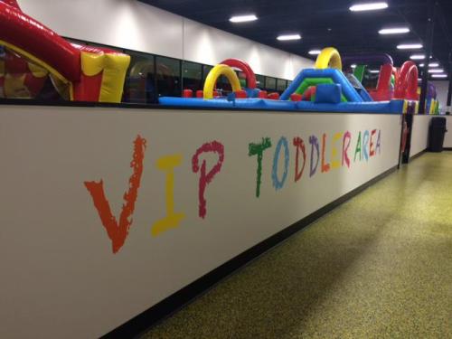 Colorful sign reading "VIP TODDLER AREA" on a wall, with inflatable play structures visible in the background.