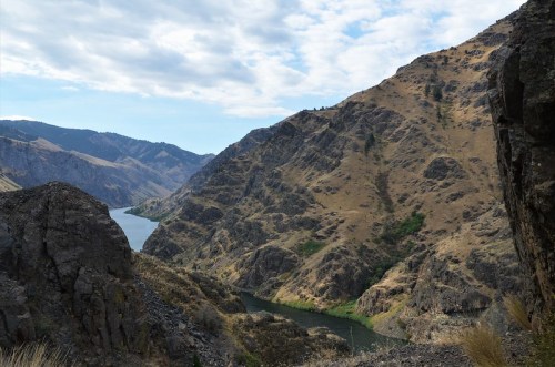 A winding river flows through rugged, rocky mountains under a partly cloudy sky.
