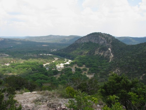 A panoramic view of rolling hills and lush green valleys under a partly cloudy sky.