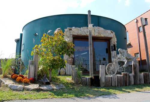 A unique round building with stone accents, surrounded by greenery and a bicycle sculpture in front.