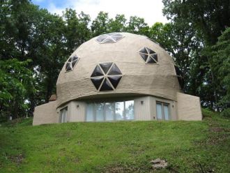 A unique dome-shaped house with large star-shaped windows, set on a grassy hillside surrounded by trees.