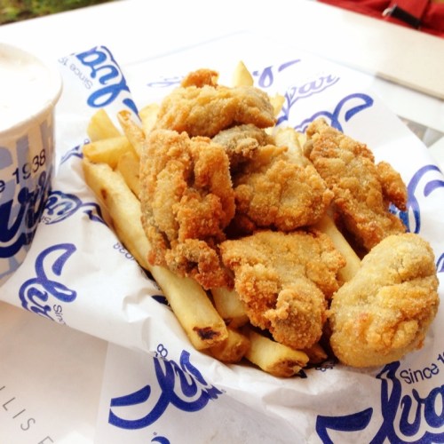 A serving of crispy fried chicken pieces on a bed of golden French fries, served in a paper basket.