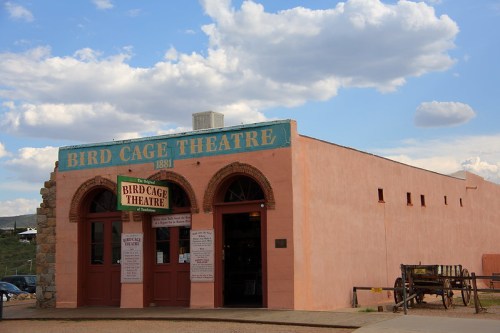 Historic Bird Cage Theatre building with a pink exterior and arched windows, set against a blue sky with clouds.