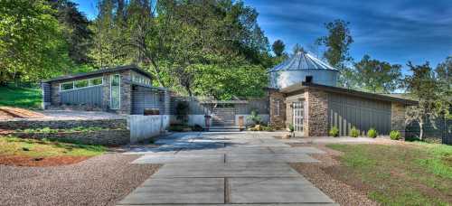 Modern architectural home surrounded by greenery, featuring stone and metal elements with a landscaped pathway.