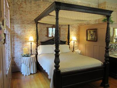 A cozy bedroom featuring a four-poster bed, warm lighting, and exposed brick walls, creating a charming atmosphere.