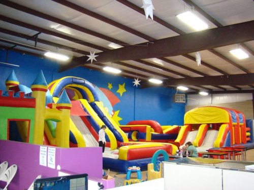 Colorful indoor bounce house area with various inflatable slides and structures, under a high ceiling.
