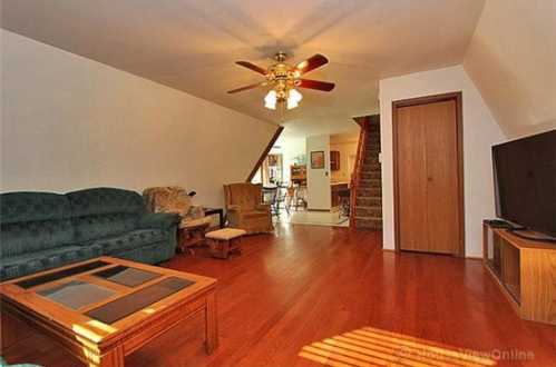 Cozy living room with a ceiling fan, green couch, wooden flooring, and a staircase in the background.