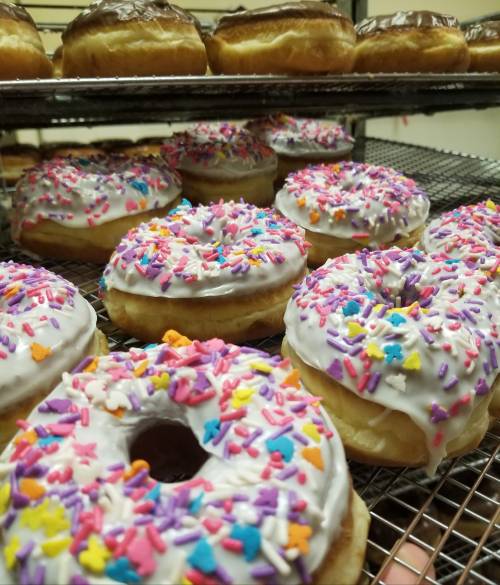 A close-up of freshly baked donuts with white icing and colorful sprinkles on a wire rack.