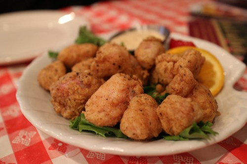 A plate of golden-brown fried chicken pieces served on lettuce with a slice of orange and dipping sauce.
