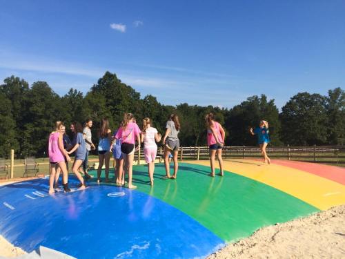 A group of girls playing on a colorful inflatable bounce pad under a clear blue sky.