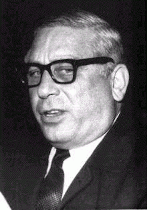 Black and white portrait of a man with glasses, wearing a suit and tie, looking slightly to the side.
