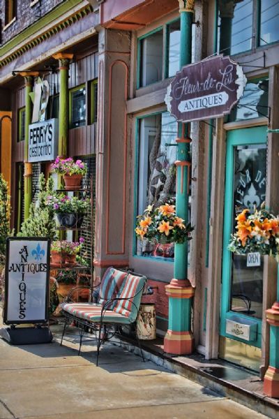 Charming antique shop entrance with colorful decor, flowers, and a sign reading "Antiques" in a quaint street setting.