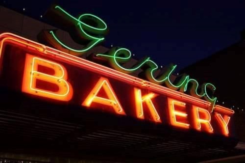 Neon sign for "Gering Bakery" illuminated at night, featuring vibrant green and orange colors.