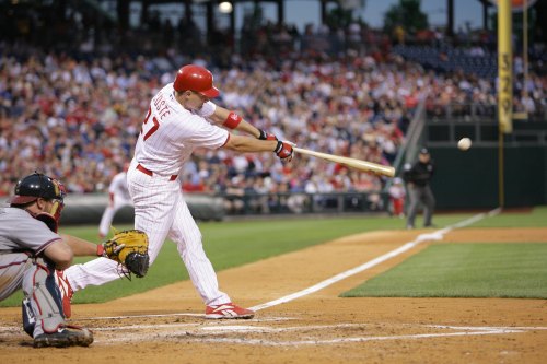 A baseball player swings a bat at home plate, with a catcher and a crowd in the background.