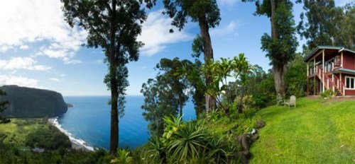 A scenic view of a coastal landscape with lush greenery and a house overlooking the ocean under a clear blue sky.