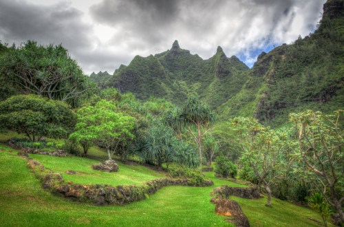 Lush green landscape with rocky formations and mountains under a cloudy sky.