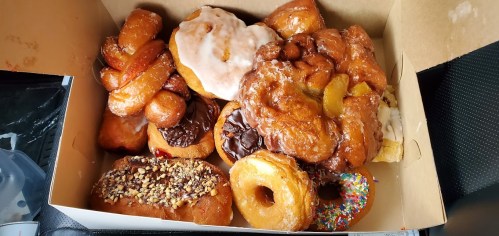A box filled with various donuts, including glazed, chocolate-covered, and sprinkled varieties.