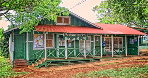 A green wooden post office building with a red roof, surrounded by trees in Manawalu, Hawaii.