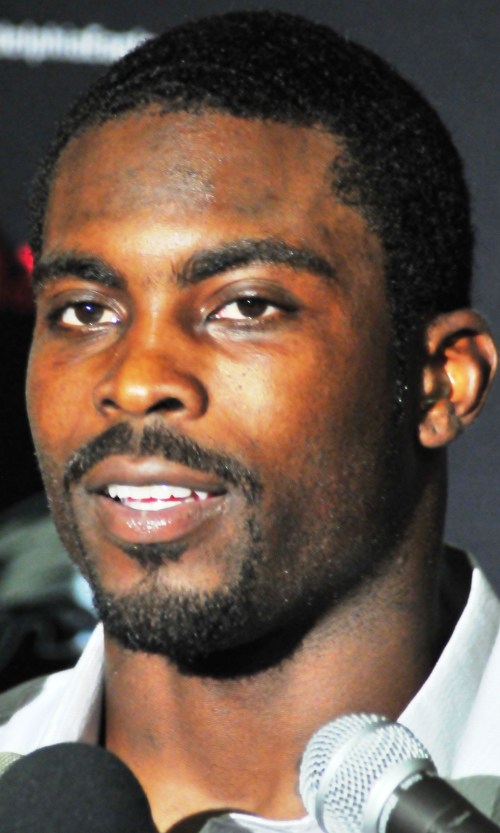 A close-up of a man speaking at a microphone, smiling, with a blurred background.
