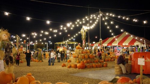 A festive night scene at a pumpkin patch, with string lights, hay bales, and people enjoying the autumn atmosphere.