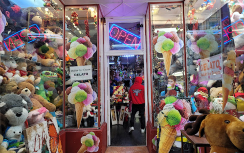 A colorful shop filled with stuffed animals and ice cream decorations, with a person in a red hoodie entering.