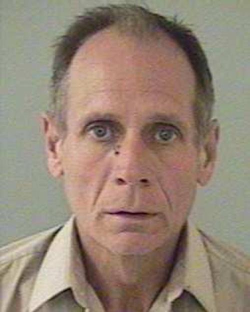 Mugshot of a middle-aged man with short hair and blue eyes, wearing a light-colored shirt, against a plain background.