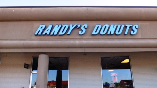 Sign for Randy's Donuts on a building exterior, featuring blue lettering against a beige background.