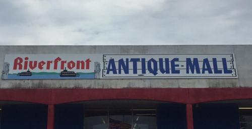 Sign for "Riverfront Antique Mall" with a graphic of boats, set against a cloudy sky.