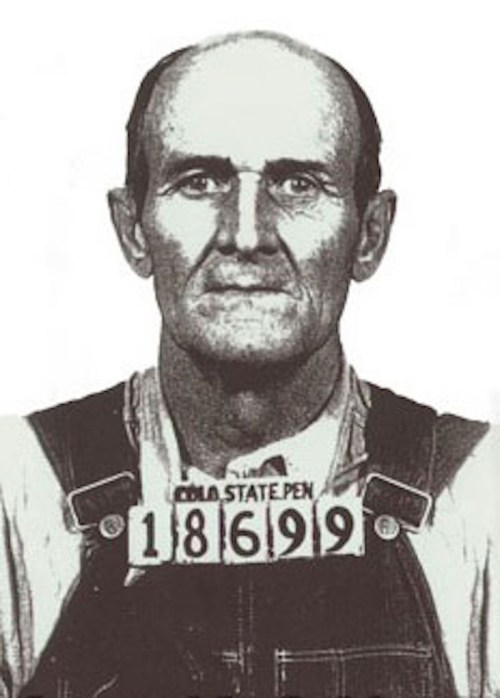 Black and white mugshot of a man in overalls, with a prison ID number 18699 displayed on his chest.