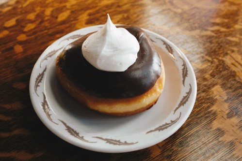 A chocolate-covered donut with a swirl of whipped cream on top, served on a decorative plate.