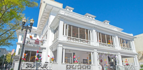 A large white building with multiple balconies and colorful decorations, set against a clear blue sky.