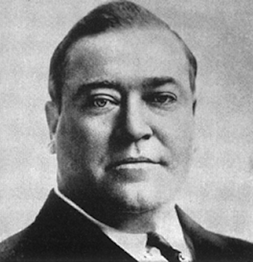 Black and white portrait of a man in a suit, with short hair and a serious expression.