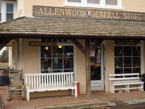 Exterior of Allenwood General Store featuring a wooden bench, signs for sandwiches and antiques, and a rustic facade.