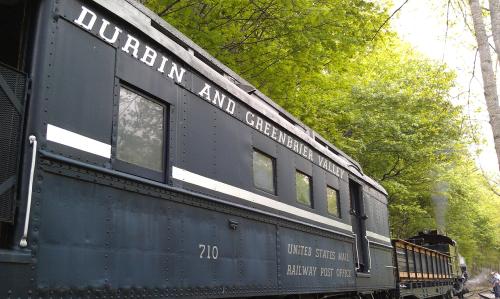 A vintage train car labeled "Durbin and Greenbrier Valley" surrounded by lush green trees.