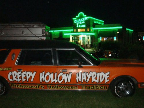 A spooky car with "Creepy Hollow Hayride" signage parked outside a brightly lit restaurant at night.