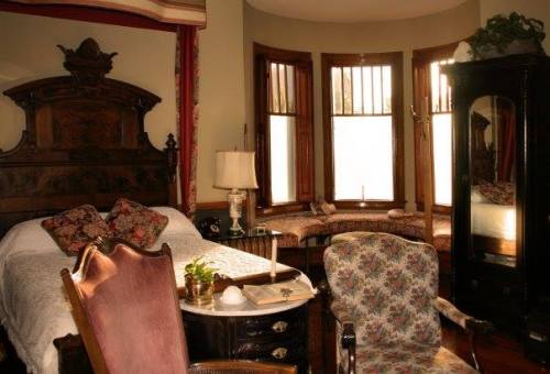 Cozy bedroom with a vintage bed, floral armchair, and a sunny bay window seating area.