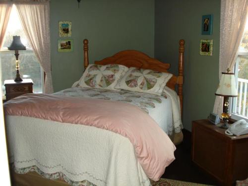 Cozy bedroom with a wooden bed, floral bedding, and soft lighting from lamps, featuring green walls and framed pictures.