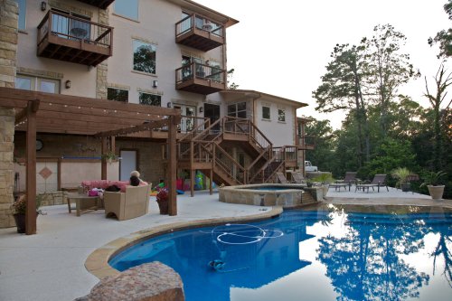 A serene backyard with a pool, lounge chairs, and a multi-level house surrounded by trees at sunset.