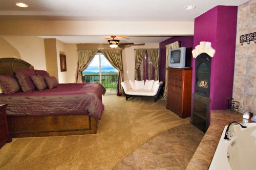 Spacious bedroom with a king bed, seating area, fireplace, and large windows showcasing a scenic view.