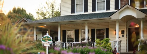 A charming house with a porch, surrounded by colorful flowers and a sign that reads "Amherst Inn."