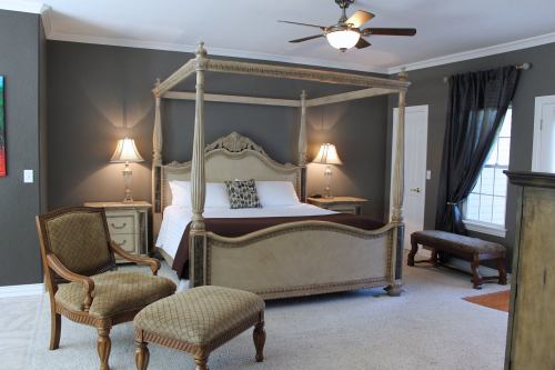 A spacious bedroom featuring a four-poster bed, elegant chairs, and soft lighting against a dark wall.