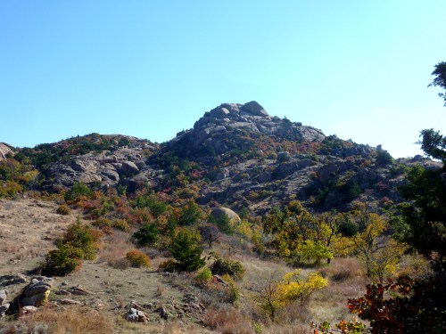 A rocky hill surrounded by autumn foliage under a clear blue sky.