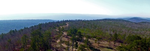A panoramic view of rolling hills and a winding path through a forested landscape under a clear sky.