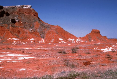 A vibrant red rock formation under a clear blue sky, with sparse vegetation in the foreground.