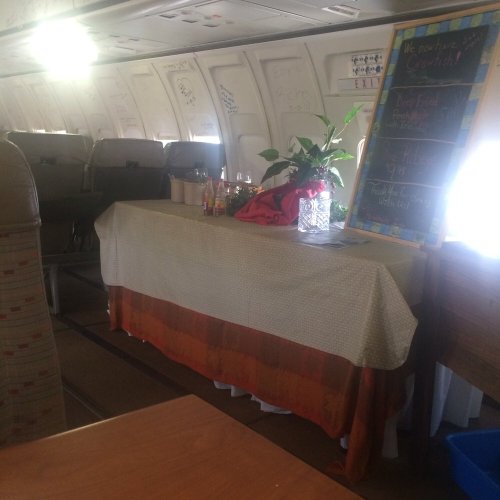 Interior of an airplane with a table set up, featuring drinks and a plant, and a chalkboard menu nearby.