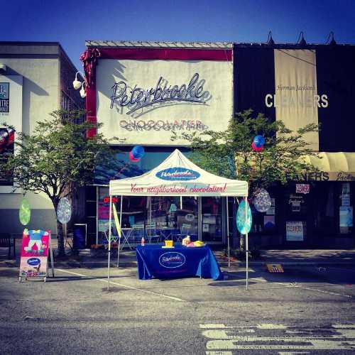 A storefront with a sign reading "Peterbrooke Chocolatier," featuring a tent and decorations for a local event.