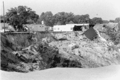 A black and white image showing a collapsed area with damaged buildings and eroded land.